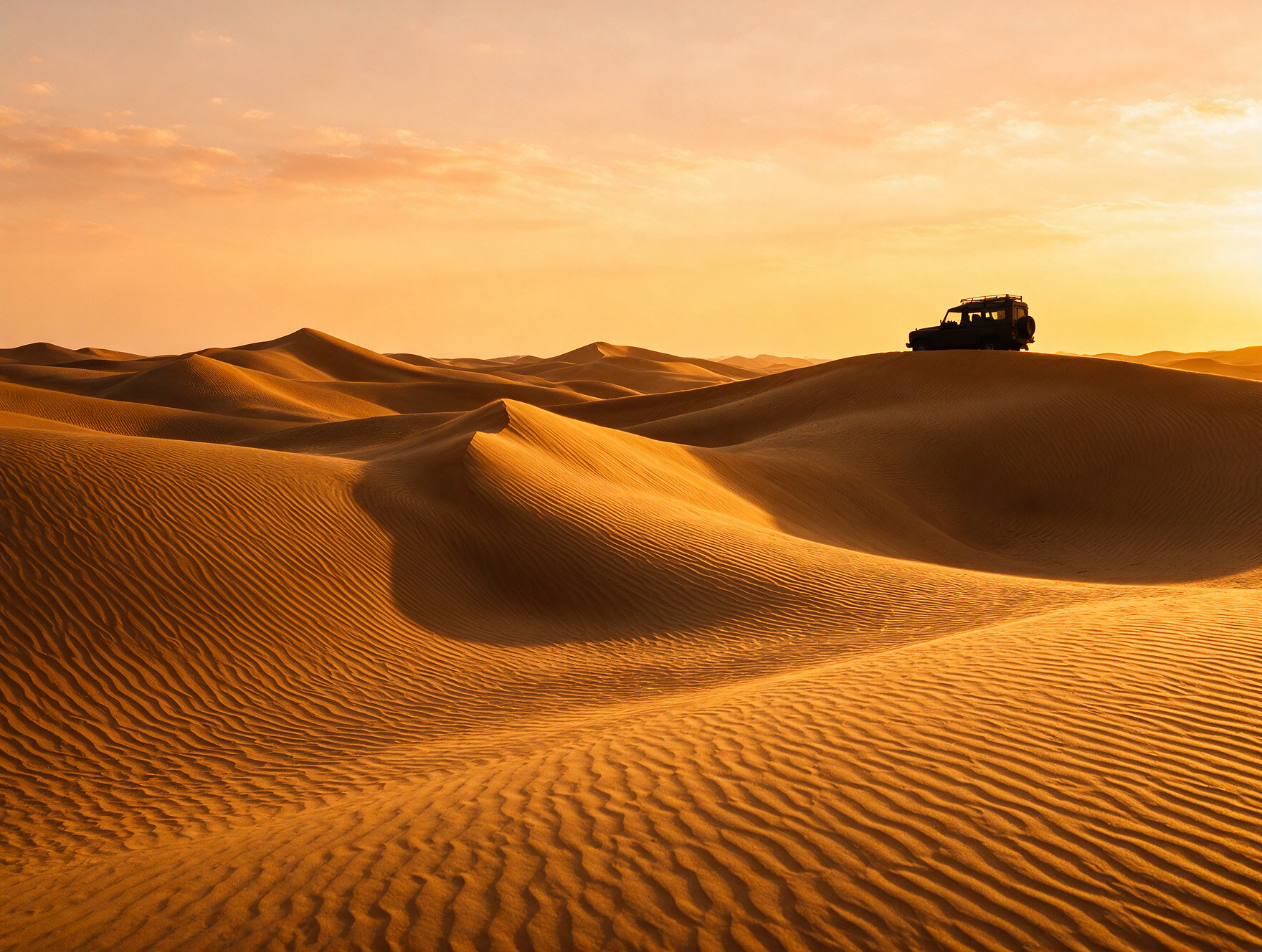 Golden sand dunes near Dubai at sunset with a 4x4 vehicle silhouette