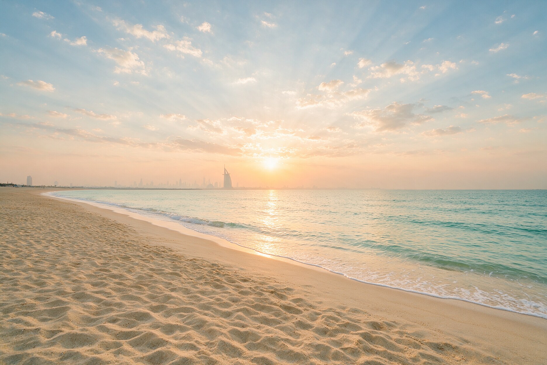 Sunrise over a public Dubai beach with the city skyline visible in the distance and calm turquoise water