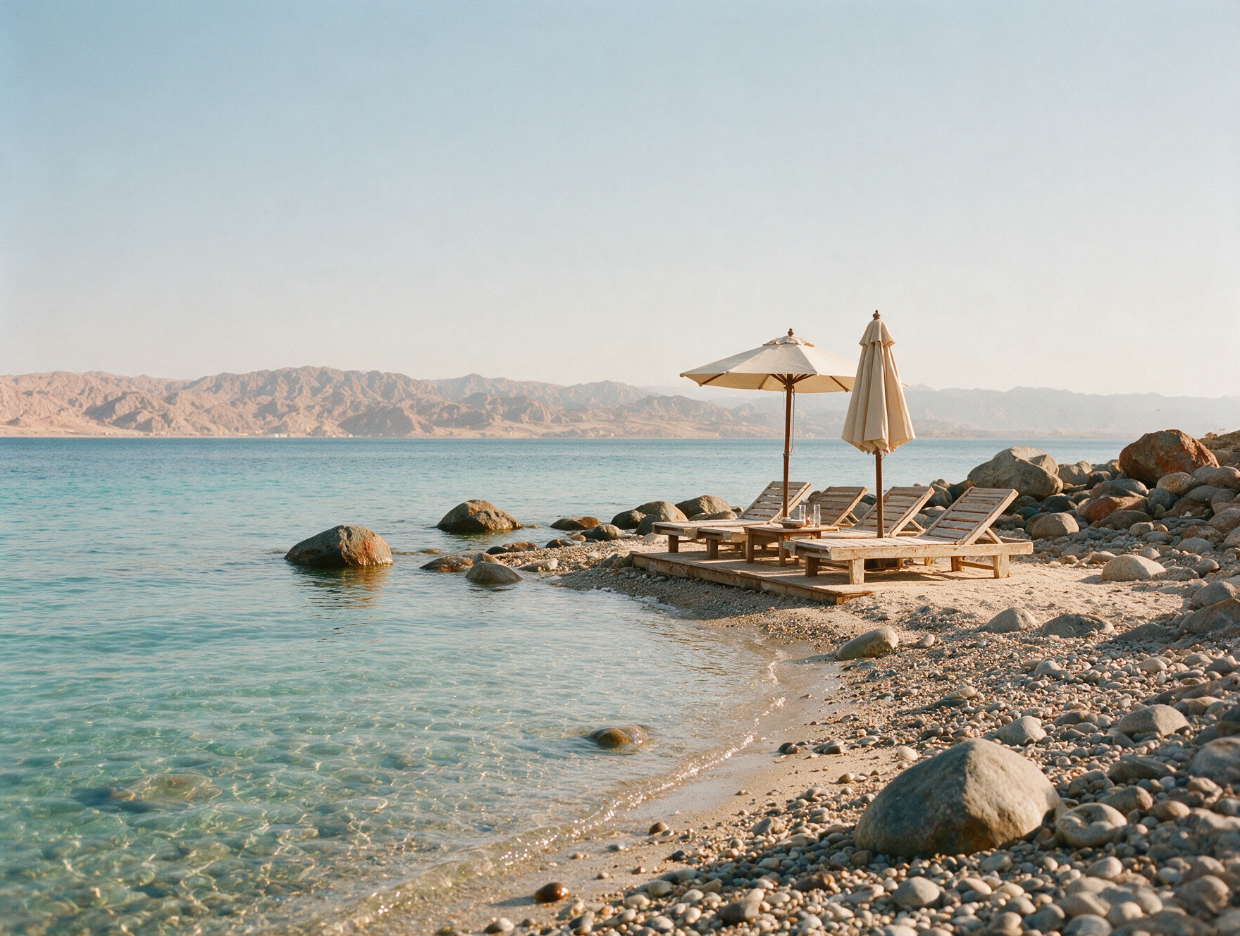Calm, nearly empty cove on the Gulf of Aqaba with sun loungers and desert mountains in the background