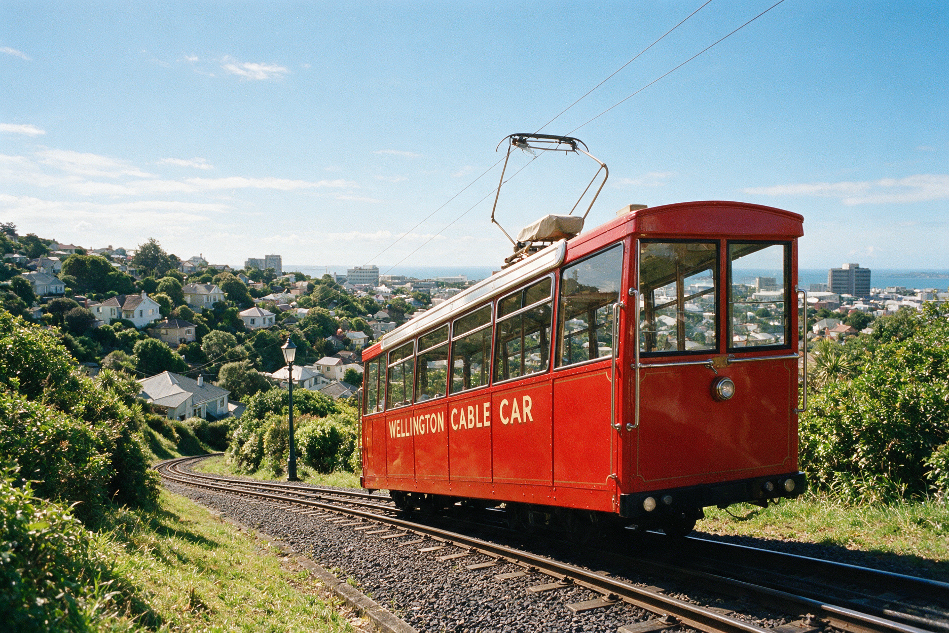 Historic red Wellington Cable Car ascending a green hillside with city views